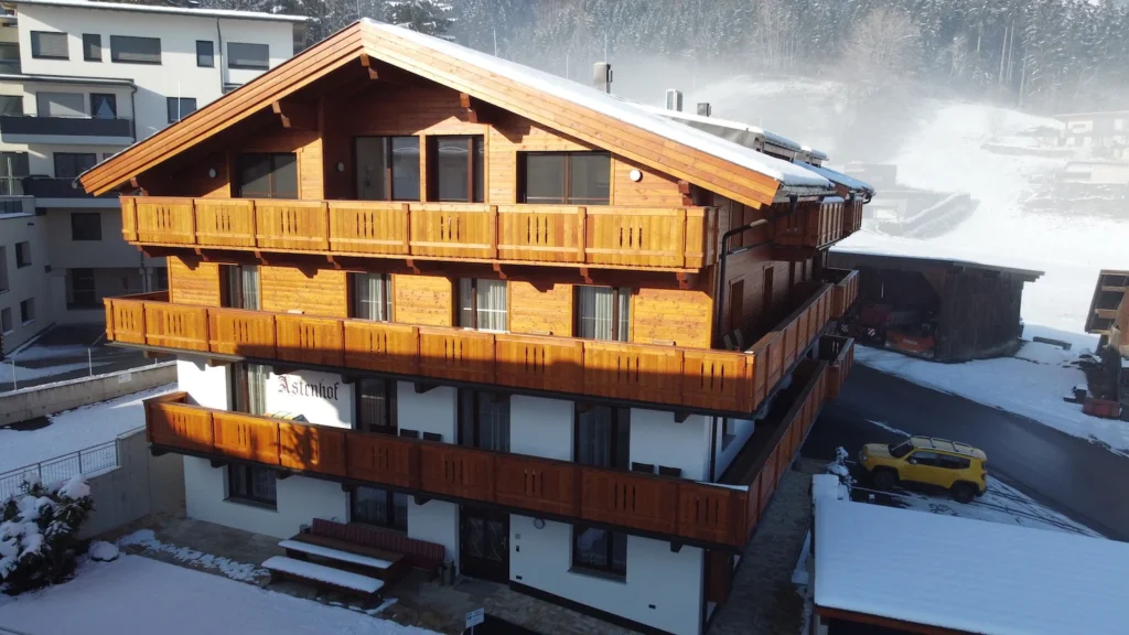 Traditionelles Tiroler Chalet im Winter, eingefangen bei einem Drohnenflug mit verschneiter Landschaft im Hintergrund